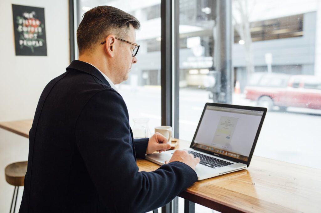 pexels-photo-2182969 Adult male in cafe working on laptop, drinking coffee. Bright workspace with street view.